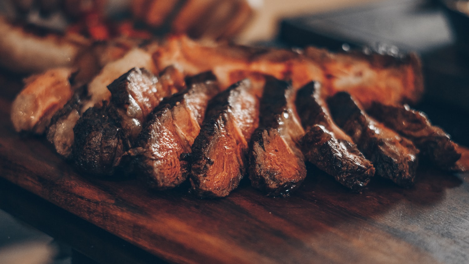 Carne selada na brasa, fatiada sobre tábua de madeira, banhada pela luz quente do fogo.