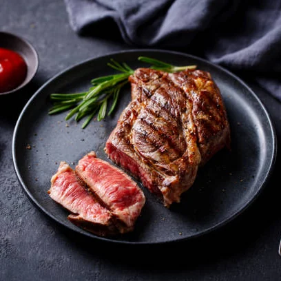 Bife grelhado, fatiado, no ponto, sobre prato preto.